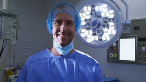 Portrait-of-smiling-male-caucasian-surgeon-with-face-mask-and-scrubs-in-hospital