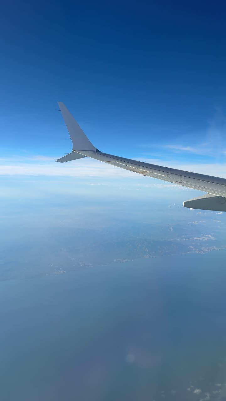 Flyvinge over hav og kystlinje set fra vinduet.