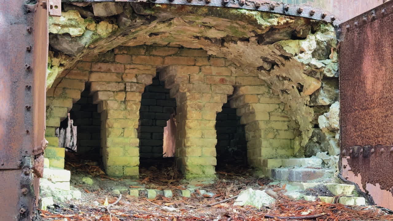 Fixed shot of historic lime kiln interior in Big Sur, showing stone arches, ground, and surrounding vegetation - California - USA
