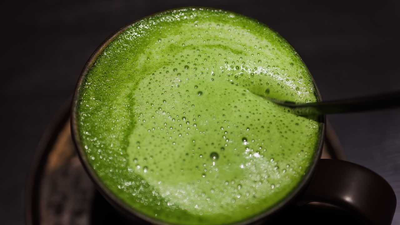 Close up of a spoon mixing into a matcha latte on a tray at a cafe
