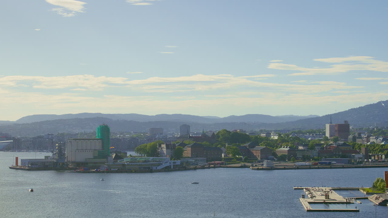 Panoramic view of a coastal city featuring industrial sites, waterfront docks, and lush green hills in the background. Filmed on a sunny summerday.