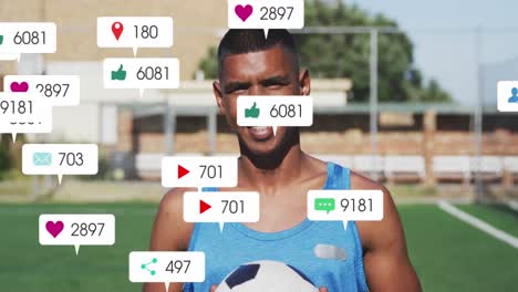 Animation-Von-Social-Media-Symbolen-über-Einem-Biracial-Männlichen-Fußballspieler-Mit-Fußball-Auf-Dem-Sportplatz