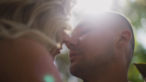 loving groom kisses blonde woman holding bouquet in park