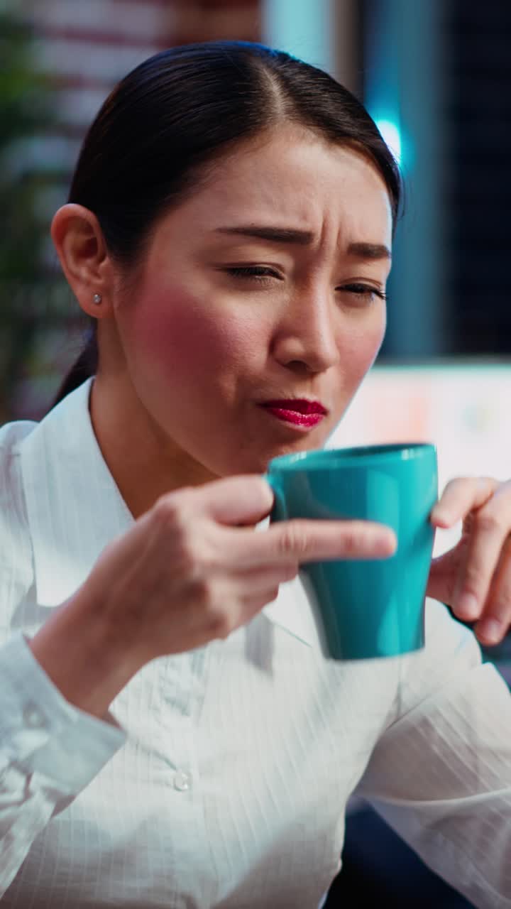 Vertical video Exhausted worker working overnight, typing on laptop, drinking coffee