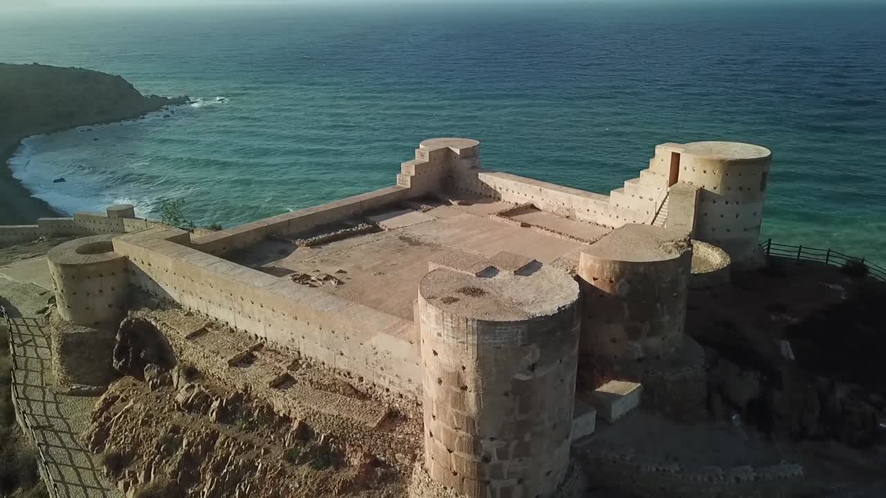 A sweeping drone shot of an historic coastal citadel placed against the expansive blue backdrop of the Mediterranean Sea horizon. A strategic defensive location