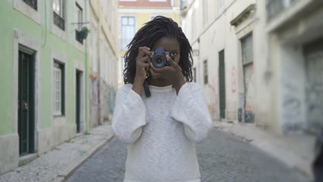 smiling female photographer taking pictures on old city street.