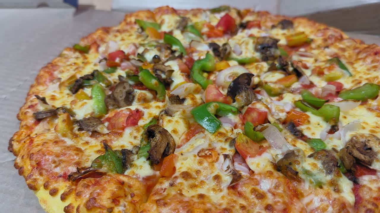 Inquadratura con camera in orbita attorno a una pizza di verdure appena sfornata, guarnita con formaggio, peperoni, cipolle, pomodori e funghi; la crosta dorata è visibile mentre la camera ruota fluidamente