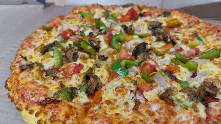 Inquadratura con camera in orbita attorno a una pizza di verdure appena sfornata, guarnita con formaggio, peperoni, cipolle, pomodori e funghi; la crosta dorata è visibile mentre la camera ruota fluidamente