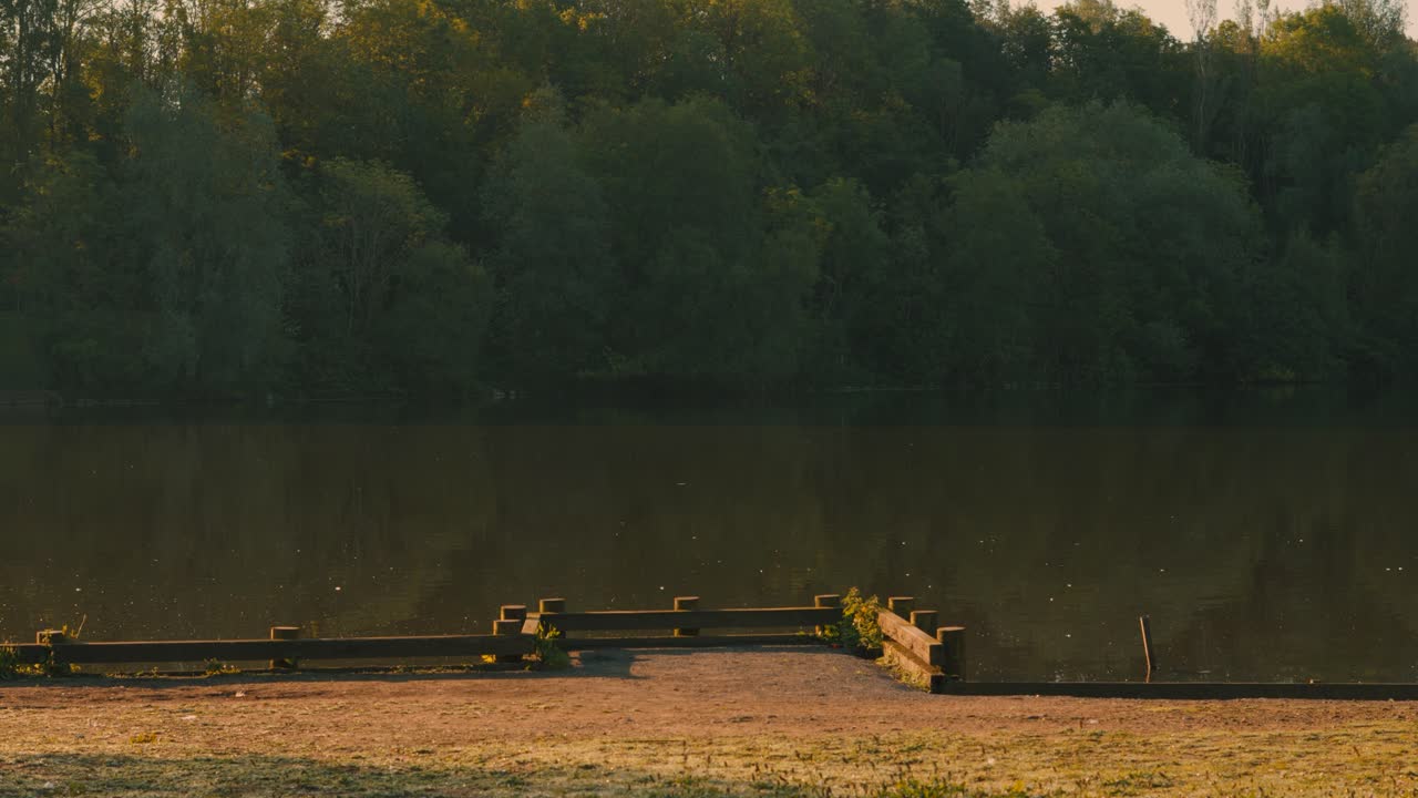 vista serena del lago tranquilo al amanecer con un pequeño muelle con árboles en el fondo del bosque