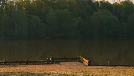 Ruhiger-Blick-Auf-Den-Stillen-See-Bei-Sonnenaufgang-Mit-Kleinem-Steg-Mit-Bäumen-Und-Waldhintergrund