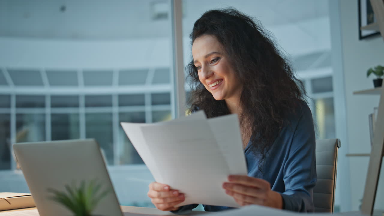 Joyful businesswoman reading documents at buro. Smiling boss working evening
