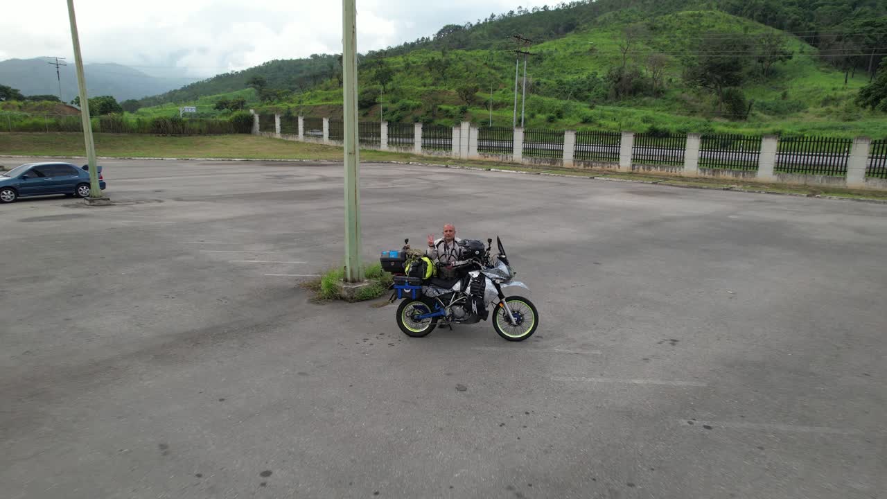 Drone shot, zoom out a lone biker and their motorcycle alongside rest of the road with lush vegetation Background