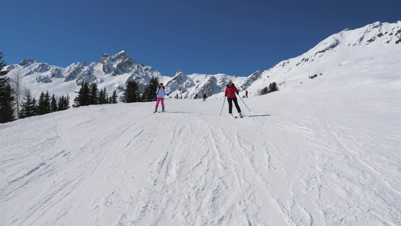 두 명의 스키 선수 여성이 함께 근처의 산 경사에서 스키 조각 스타일을합니다.
