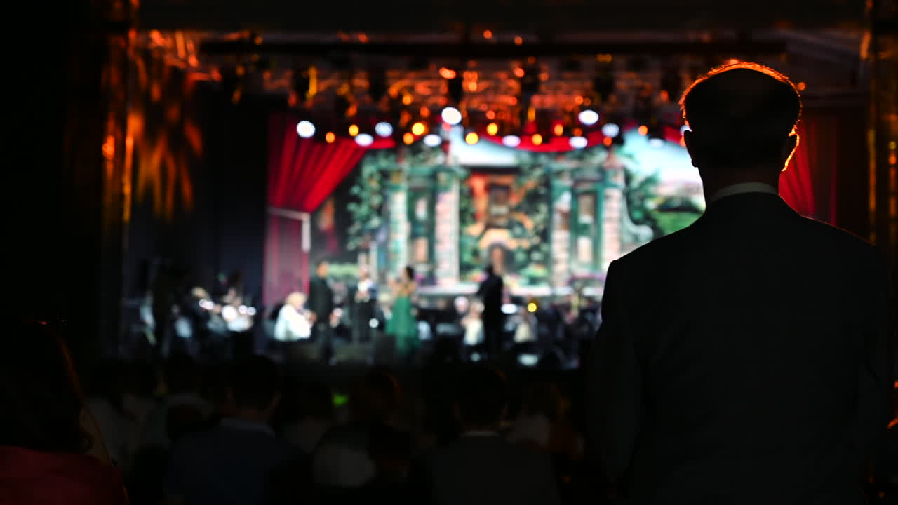 Crowd enjoys a vibrant live performance featuring an orchestra and skilled vocalists. The enchanting atmosphere is filled with music and lively lights under a beautiful night sky