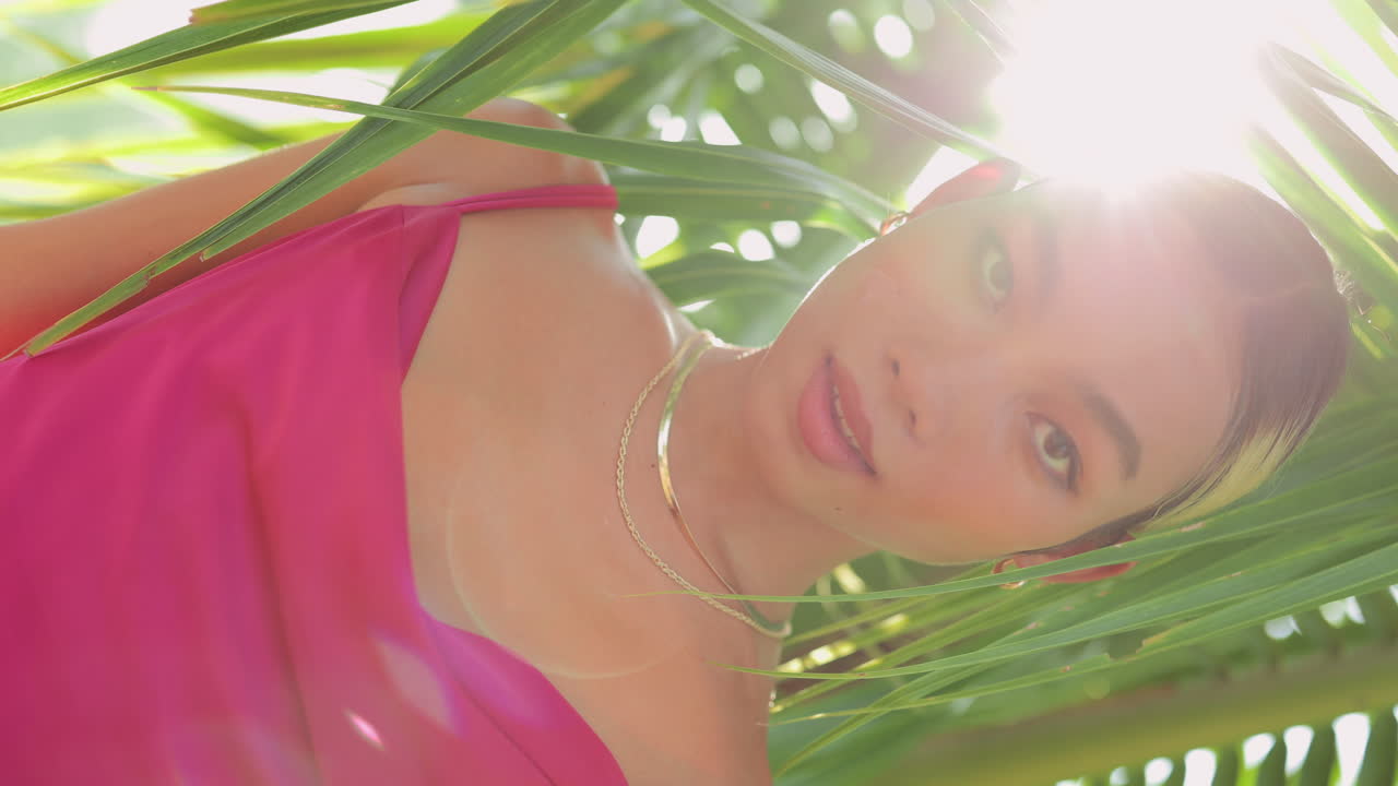 Confident woman in pink dress among palm leaves