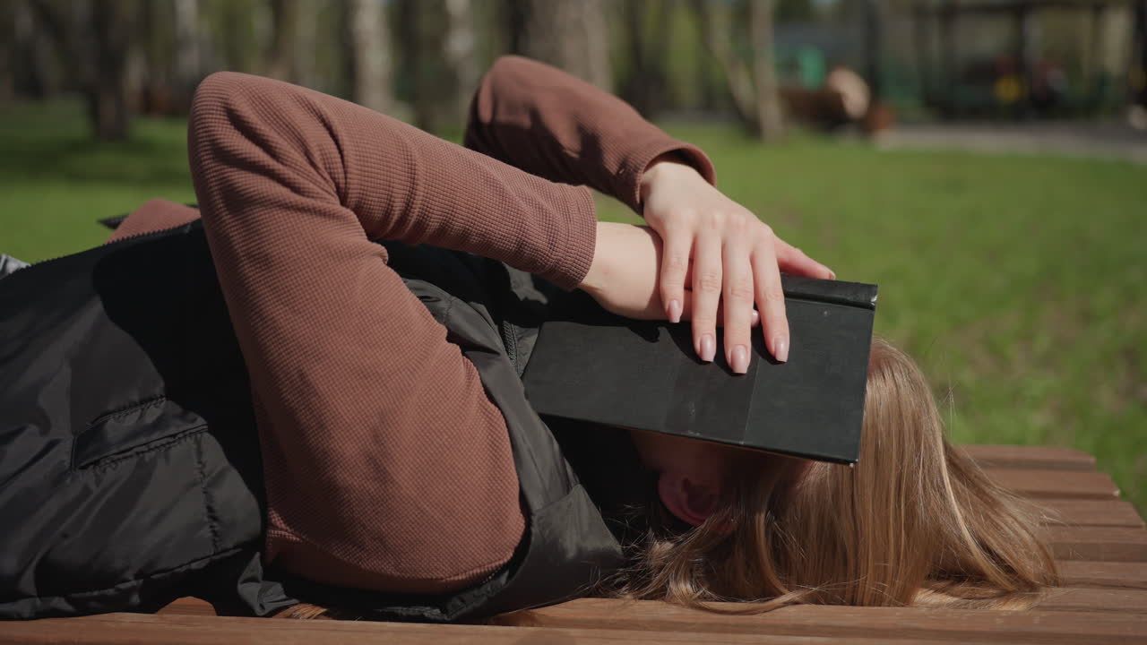 Расслабленный студент наслаждается перерывом в солнечном парке, молодой человек мирно лежит на деревянной скамейке на улице, спокойный студент отдыхает на скамейке в парке в солнечный полдень, расслабляясь на природе