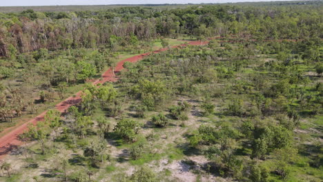 High-Moving-aerial-drone-shot-of-Red-Winding-Road-and-Dense-Green-Bushland-near-Holmes-Jungle-Nature-Park,-Darwin,-Northern-Territory