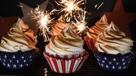 Bengalas-Que-Explotan-Alrededor-De-Cupcakes-Rojos,-Blancos-Y-Azules-Con-La-Parte-Superior-De-Remolino-De-Merengue-Tostado