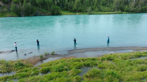 Aerial-drone-reveal-of-Alaskan-fisherman-wading-on-shoreline-casting-a-line-fly-fishing-for-Sockeye-and-King-Salmon-in-pristine-blue-river-water