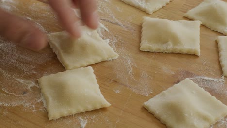 hands using fluted pastry wheel to cut ravioli pieces on floured table