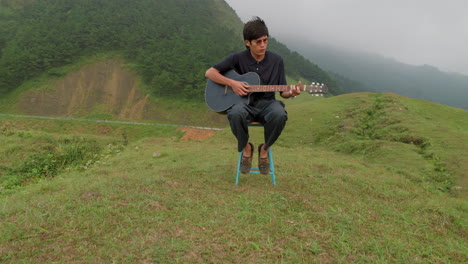 Un-Joven-Asiático-Clásico-Tocando-La-Guitarra-En-Lo-Alto-De-Montañas-Verdes-Exóticas