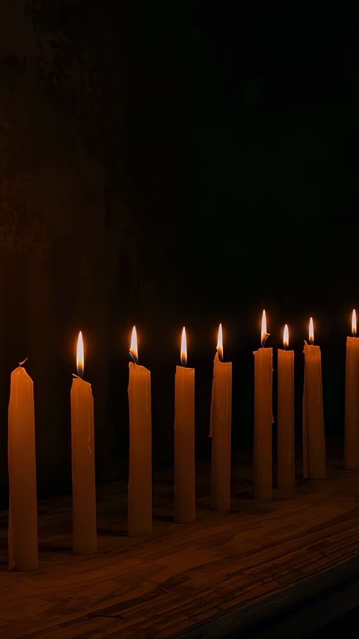 Vertical video: Camera panning across wooden ledge before dark wall showing flickering wax candles