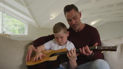 Kaukasischer-Vater-Und-Sohn-Spielen-Gemeinsam-Gitarre-Und-Sitzen-Im-Wohnzimmer