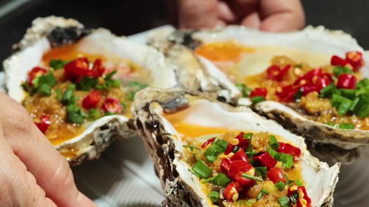Close-up of hands holding a tray of oysters garnished with red and green chilies