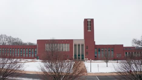 Rising-drone-aerial-shot-of-large-brick-school,-college,-university-covered-in-snow