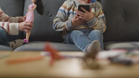 Close-Up-Of-Girl-Playing-With-Toy-Doll-As-Boy-Uses-Mobile-Phone