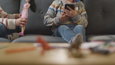 close up of girl playing with toy doll as boy uses mobile phone