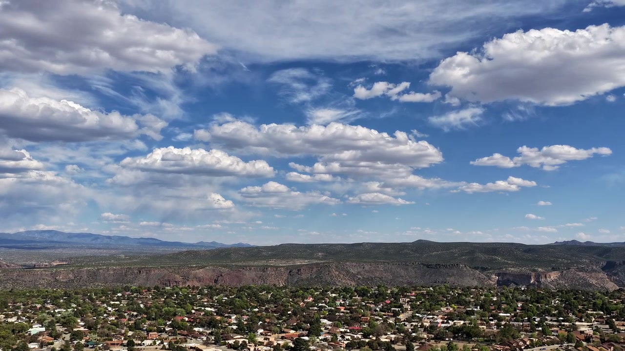 Timelapse 4K con drone utilizza un movimento ascendente fluido per rivelare nuvole mozzafiato che si muovono sopra una città canyon nel sud-ovest. Riprese aeree ascendenti catturano un vasto quartiere suburbano desertico e un panorama montano.
