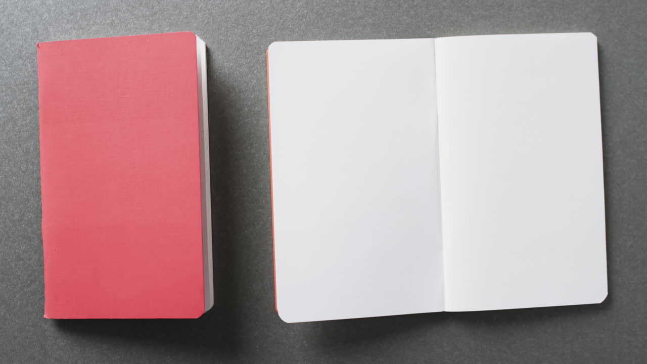 Close up of open blank book and pink book with copy space on gray background in slow motion
