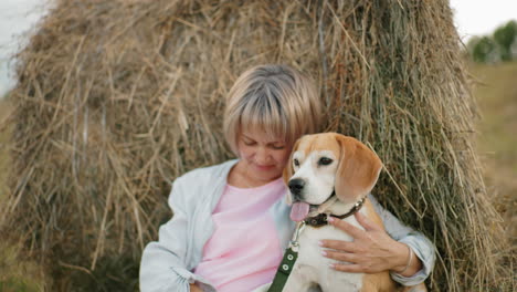 woman holds her dog closely, affectionately touching it while resting against hay bale in vast farmland, she rests her head on dog head, sharing a loving and peaceful moment in the open countryside