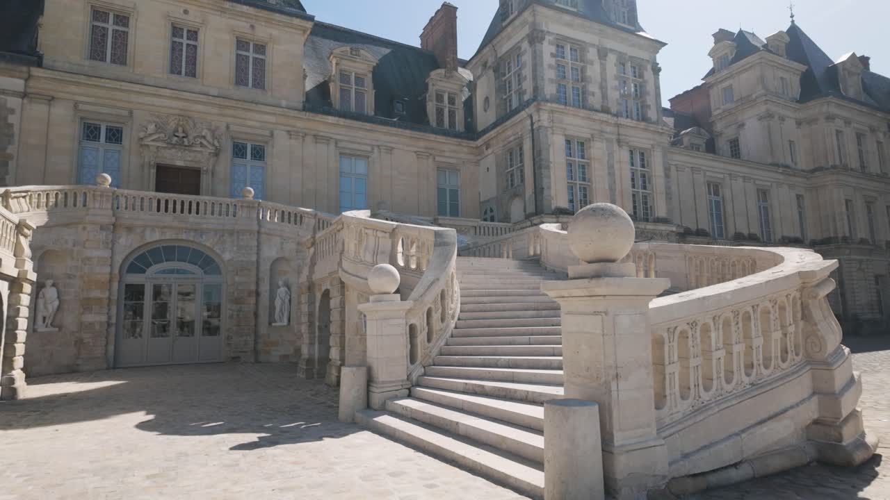 Slow-motion footage of Château de Fontainebleau near Paris, France, featuring the iconic double staircase and Renaissance palace architecture under bright daylight