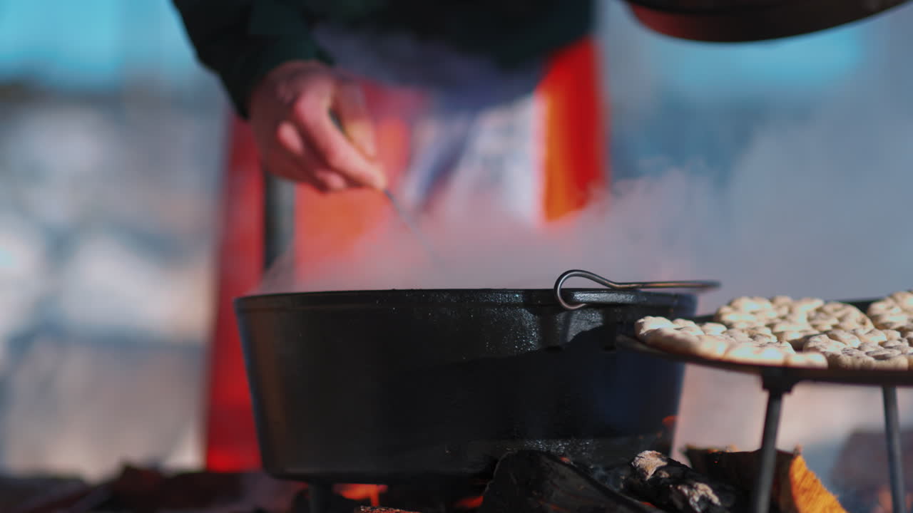 스웨덴 야외 요리에서 뜨거운 난로 위에 무스 수프의 김이 나는 냄비를 휘젓는 인간의 손