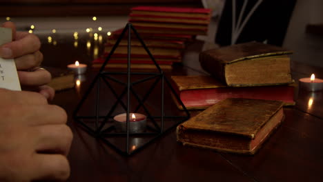 several candles are lit on the table, an iron pyramid and antique books are visible