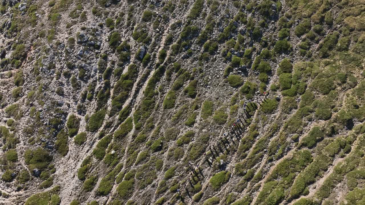 Hikers march on eroded soil of Mount Vermio in midsummer, drone orbit over stunning pattern - Greece 4k