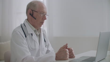 telemedicine session with cardiologist aged male doctor is sitting in his medical office and chatting online with patient and colleague