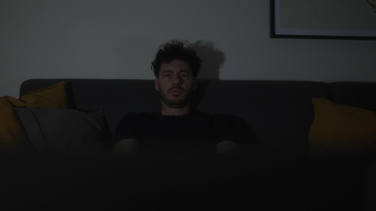 Young man with a serious expression sitting on the home sofa to watch TV