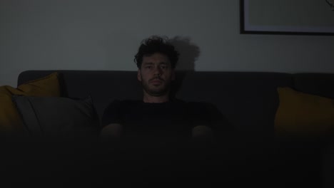 young man with a serious expression sitting on the home sofa to watch tv