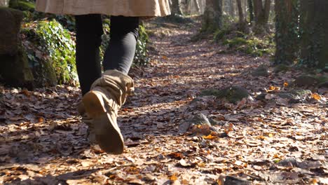 woman in brown slouch boots walking on autumn forest leaves, slowmo closeup