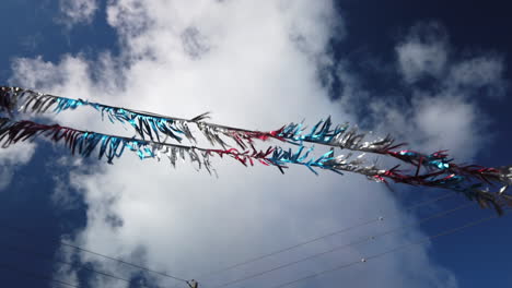 wide shot looking upwards at coloured metallic tinsel foil tassels blowing on a line