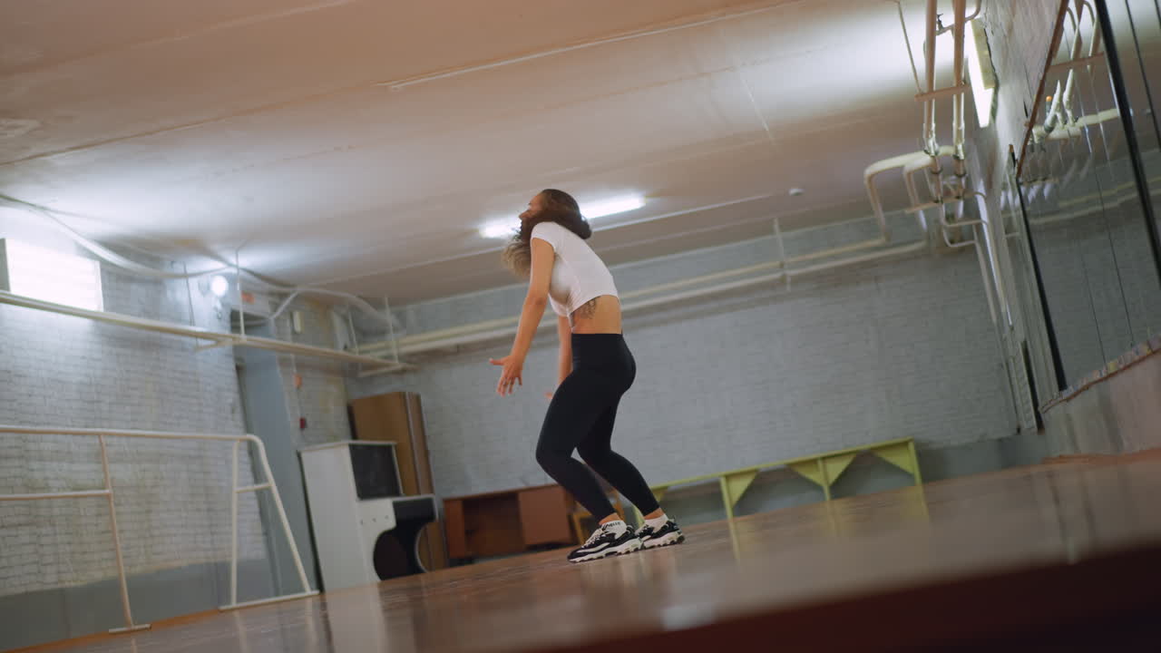 Pretty lady in white top and black leggings dancing inside fitness studio, moving body with energy, rhythm, and focus, showing graceful confident performance, expressive motion