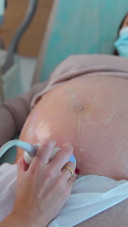 doctor's hand moves the device around big pregnant belly of a patient. obstetrician presses buttons with other hand on apparatus keyboard. vertical video