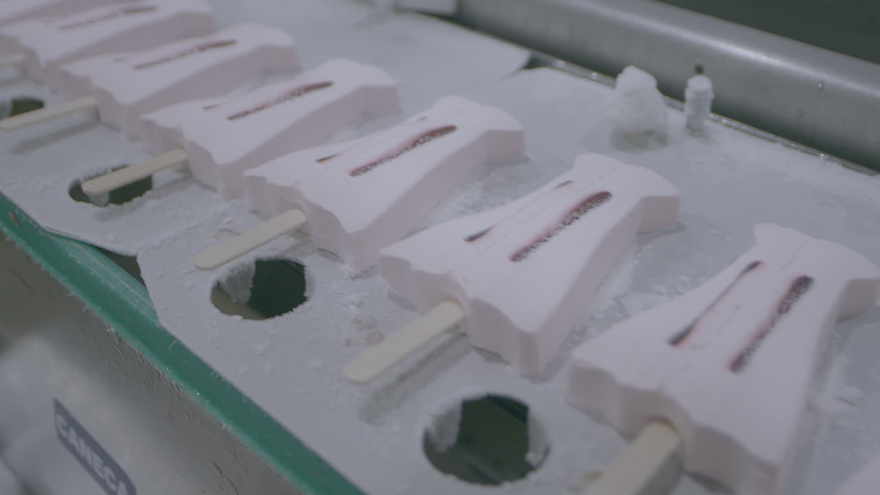 Fixed clip showing ice cream lollies on manufacturing conveyor belt moving from left to right