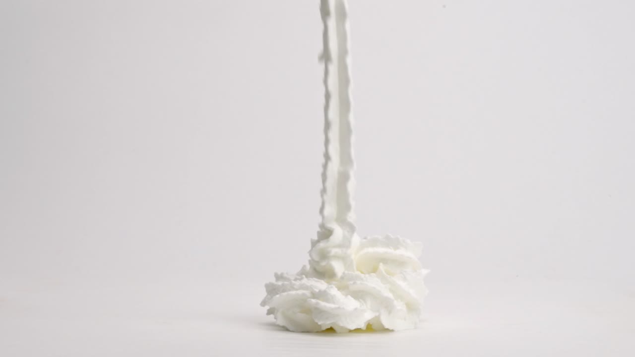замедленная съемка лент из взбитых сливок, стекающих в идеальную кучу и опрокидывающихся на белую столешницу