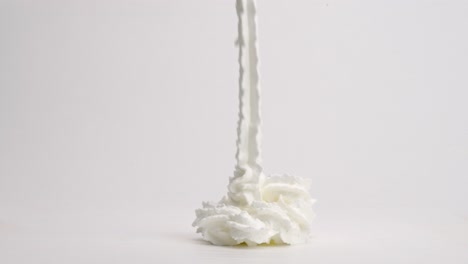 Slow-motion-whipped-cream-ribbons-raining-down-into-perfect-pile-and-toppling-over-on-white-table-top