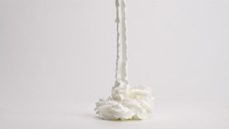 slow motion whipped cream ribbons raining down into perfect pile and toppling over on white table top