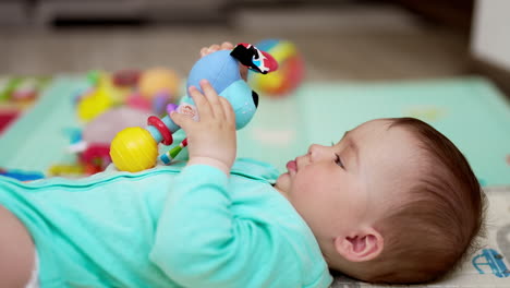 little baby boy looking earnestly on the toy in his hands. cute child waves the toy, looks into camera and shows his tongue.